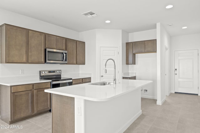 kitchen with light tile patterned flooring, sink, stainless steel appliances, and a kitchen island with sink