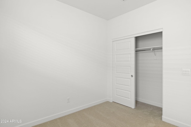 unfurnished bedroom with light colored carpet and a closet