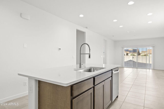 kitchen with a center island with sink, light tile patterned floors, sink, dishwasher, and dark brown cabinetry