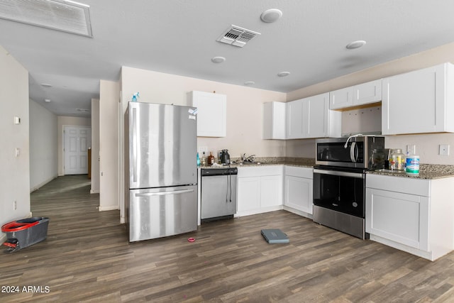 kitchen with white cabinetry, stainless steel appliances, dark hardwood / wood-style floors, and dark stone counters