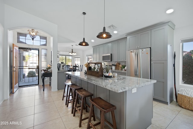 kitchen with decorative light fixtures, stainless steel appliances, gray cabinets, and light stone counters