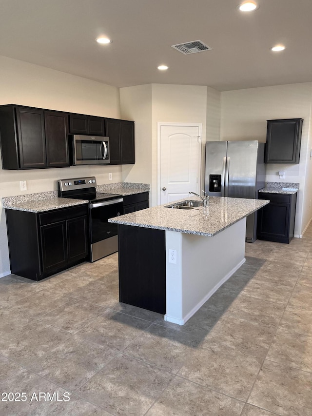 kitchen with light stone countertops, stainless steel appliances, sink, and a kitchen island with sink