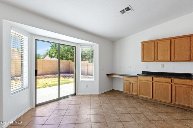 1669 E Santa Fiore St, San Tan Valley, AZ 85140 - kitchen featuring brown cabinets, dark countertops, baseboards, light tile patterned floors, and vaulted ceiling