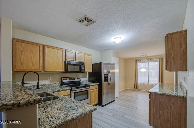 kitchen featuring light hardwood / wood-style floors, kitchen peninsula, appliances with stainless steel finishes, dark stone counters, and sink