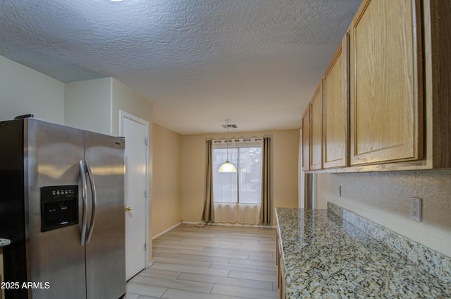 kitchen featuring stainless steel fridge, light brown cabinetry, a textured ceiling, light hardwood / wood-style flooring, and light stone counters