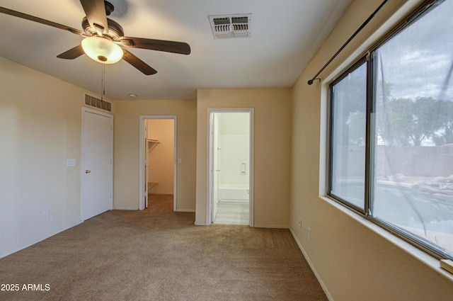 unfurnished bedroom with a spacious closet, a closet, ceiling fan, light colored carpet, and ensuite bathroom