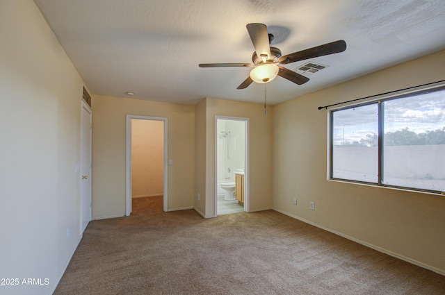 unfurnished bedroom with ensuite bath, a walk in closet, ceiling fan, and light carpet