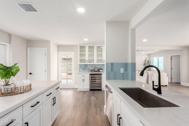 kitchen with a sink, visible vents, beverage cooler, and white cabinetry