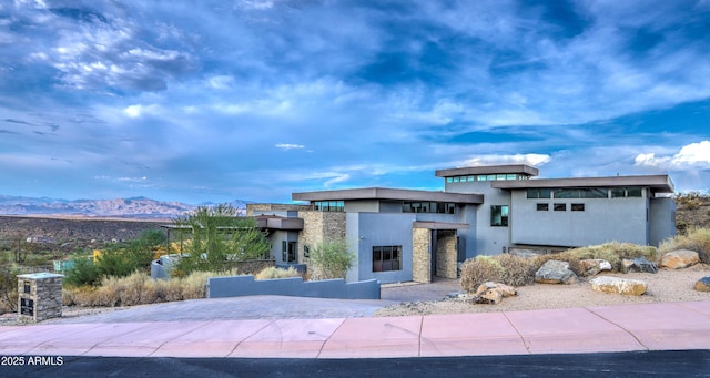 view of front of home with stone siding, a mountain view, and stucco siding