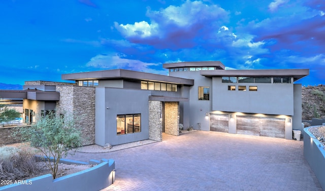 back of property with a patio, stone siding, an attached garage, decorative driveway, and stucco siding