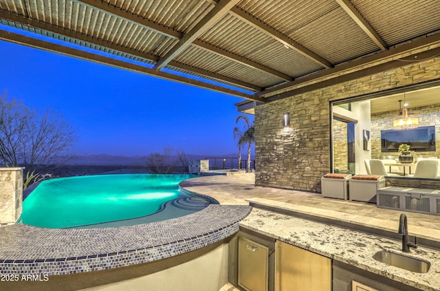 pool at dusk with a patio, an outdoor pool, a sink, and area for grilling