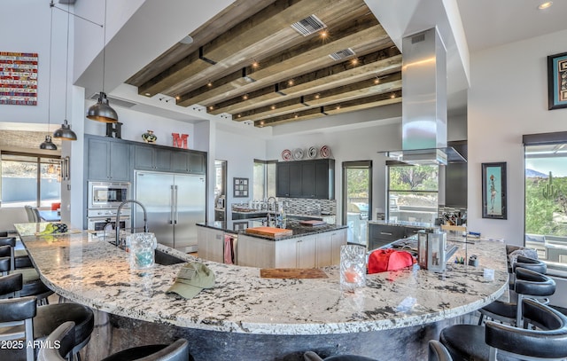 kitchen with island range hood, dark stone counters, built in appliances, a kitchen bar, and a wealth of natural light