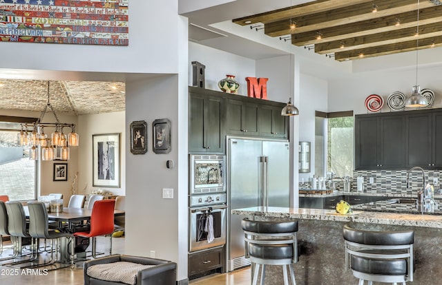 kitchen with tasteful backsplash, appliances with stainless steel finishes, light stone countertops, brick ceiling, and beamed ceiling