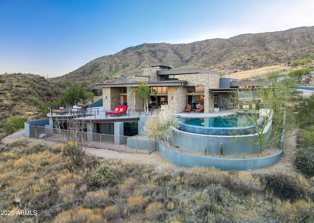 rear view of house with a mountain view, fence, stone siding, an outdoor pool, and a patio area