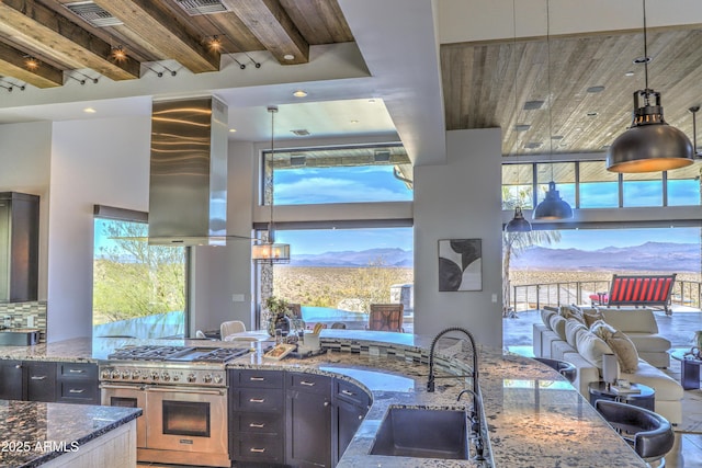 kitchen with range with two ovens, tasteful backsplash, a sink, wall chimney range hood, and dark stone countertops