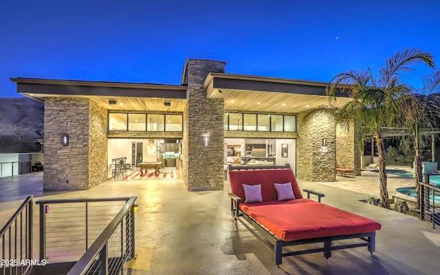 back of house featuring stone siding, a patio, a chimney, and an outdoor pool