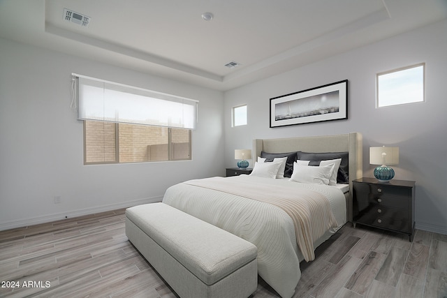 bedroom featuring light wood-type flooring, a tray ceiling, and multiple windows