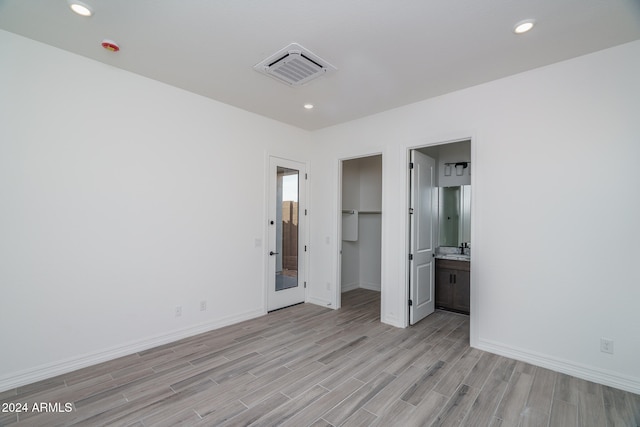 unfurnished bedroom with ensuite bathroom, a closet, light hardwood / wood-style floors, and a spacious closet