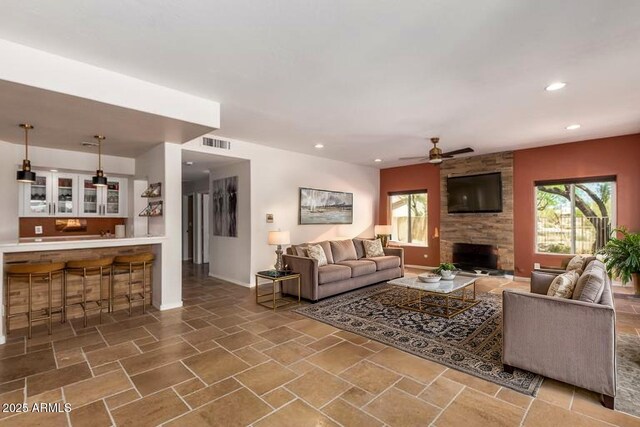 living room featuring a fireplace, a ceiling fan, recessed lighting, baseboards, and stone finish floors