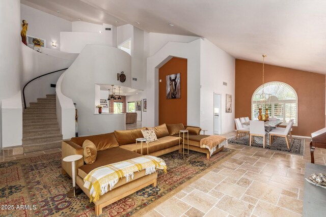 living room featuring high vaulted ceiling, stone tile floors, stairway, and a chandelier