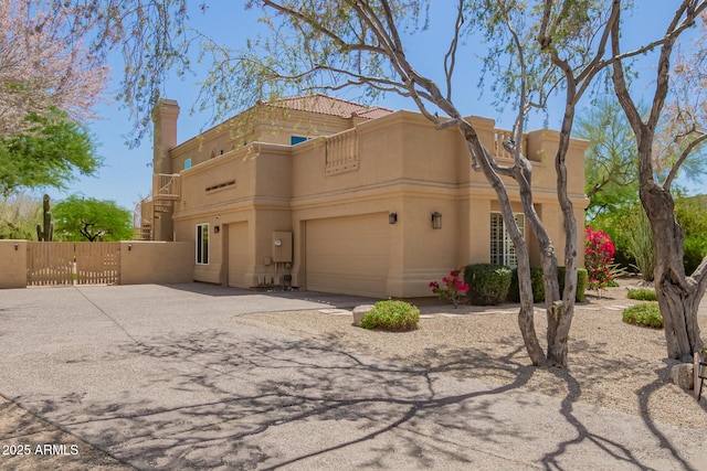view of front of property featuring a balcony, a gate, stucco siding, driveway, and fence