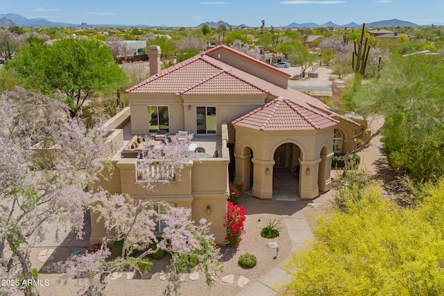 mediterranean / spanish-style house featuring stucco siding, a chimney, a mountain view, and a tile roof