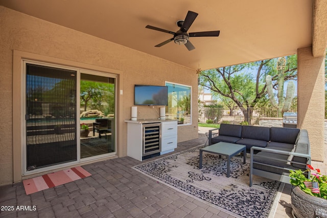 view of patio featuring beverage cooler, an outdoor kitchen, fence, an outdoor living space, and ceiling fan