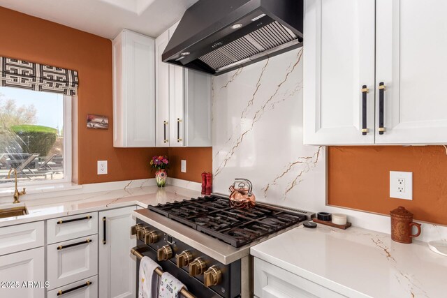 kitchen featuring wall chimney exhaust hood, gas stove, white cabinets, and light stone countertops