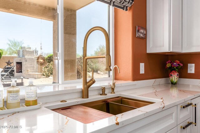 kitchen with a sink, white cabinetry, and light stone counters