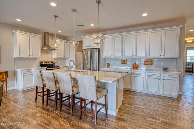 kitchen with visible vents, a breakfast bar, a sink, stainless steel appliances, and wall chimney exhaust hood