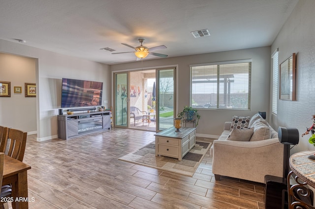 living area with visible vents, ceiling fan, baseboards, and wood finish floors