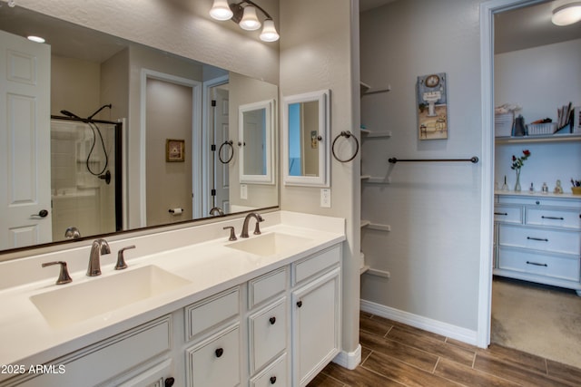 full bathroom with a sink, wood finish floors, double vanity, and a tile shower