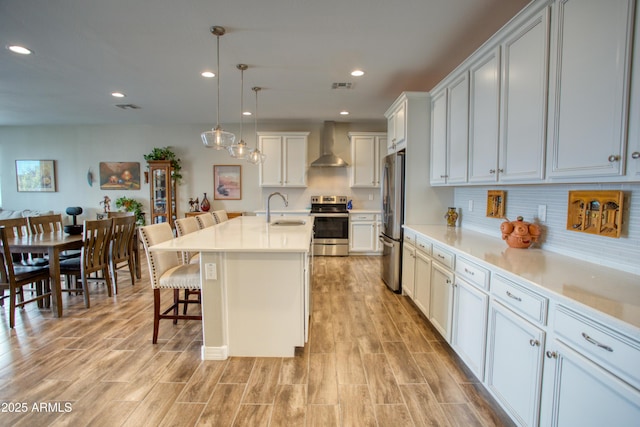 kitchen featuring visible vents, wall chimney range hood, appliances with stainless steel finishes, a kitchen breakfast bar, and a sink