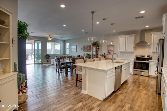 kitchen with a breakfast bar area, wood finished floors, a sink, stainless steel appliances, and wall chimney exhaust hood