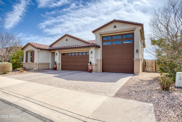 mediterranean / spanish house featuring stucco siding, driveway, a tile roof, fence, and an attached garage