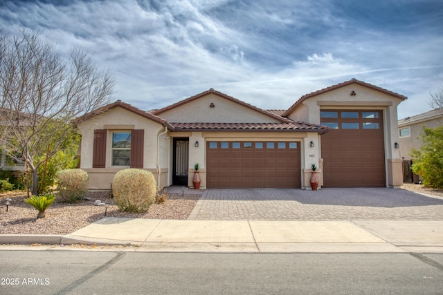 view of front of home with stucco siding, a tiled roof, decorative driveway, and a garage