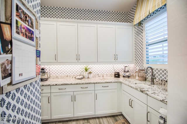 kitchen with white cabinetry, light wood-style flooring, light stone counters, and a sink