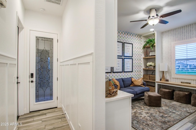 foyer with a wall mounted air conditioner, visible vents, a ceiling fan, wallpapered walls, and light wood finished floors