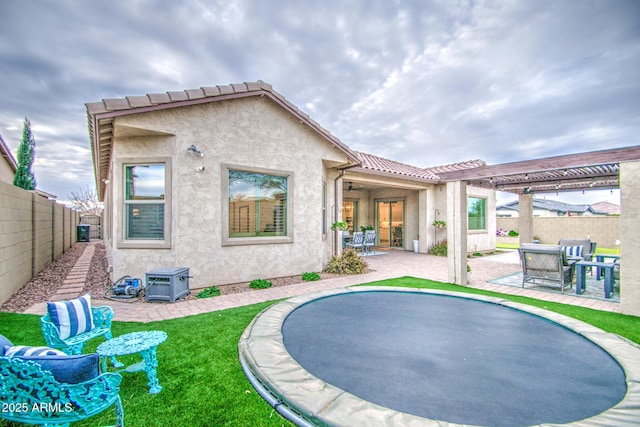 back of property featuring a patio, a fenced backyard, a pergola, stucco siding, and a trampoline