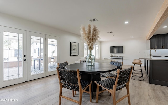 dining space with sink, light wood-type flooring, and french doors