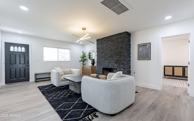 living room featuring an inviting chandelier, light hardwood / wood-style flooring, and a stone fireplace