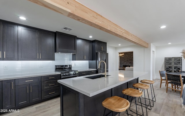 kitchen featuring beam ceiling, stainless steel gas range, and an island with sink