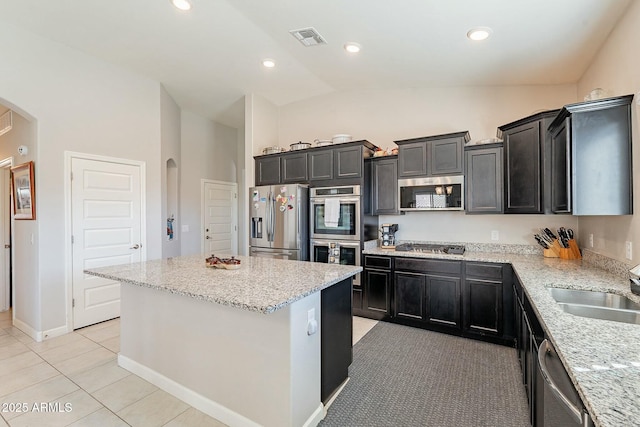 kitchen with vaulted ceiling, light tile patterned flooring, a center island, light stone counters, and stainless steel appliances