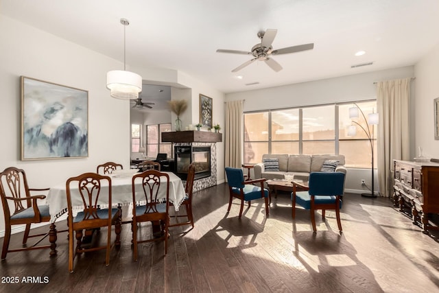 dining area featuring hardwood / wood-style flooring, a multi sided fireplace, and ceiling fan