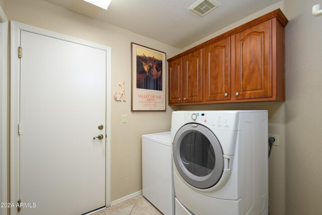 clothes washing area featuring light tile patterned floors, cabinets, and washing machine and dryer