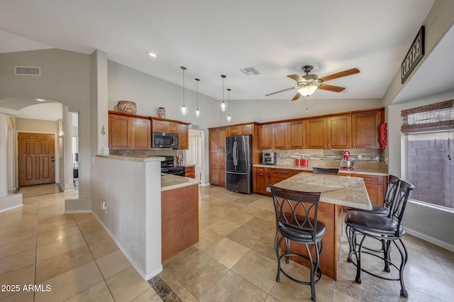 kitchen featuring lofted ceiling, a kitchen breakfast bar, hanging light fixtures, black appliances, and light stone countertops