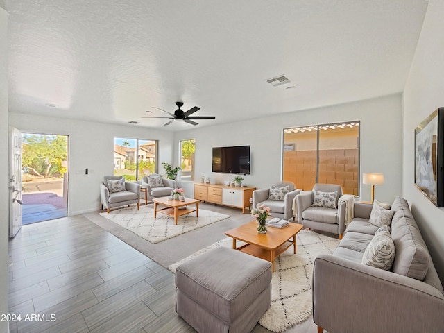 living room with ceiling fan, a textured ceiling, and light wood-type flooring