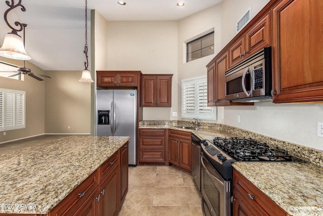 kitchen featuring ceiling fan, appliances with stainless steel finishes, light stone countertops, pendant lighting, and a sink