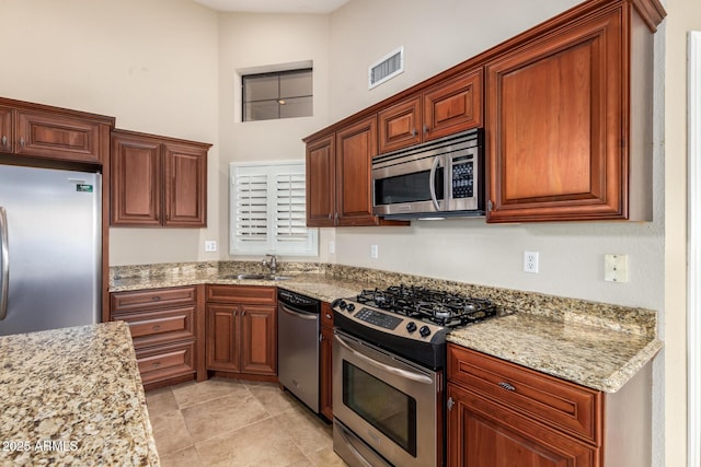 kitchen with light stone counters, stainless steel appliances, visible vents, a towering ceiling, and a sink