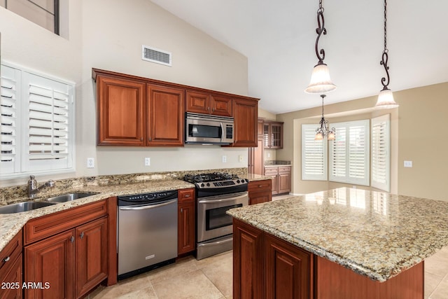 kitchen with stainless steel appliances, a sink, visible vents, a center island, and light stone countertops